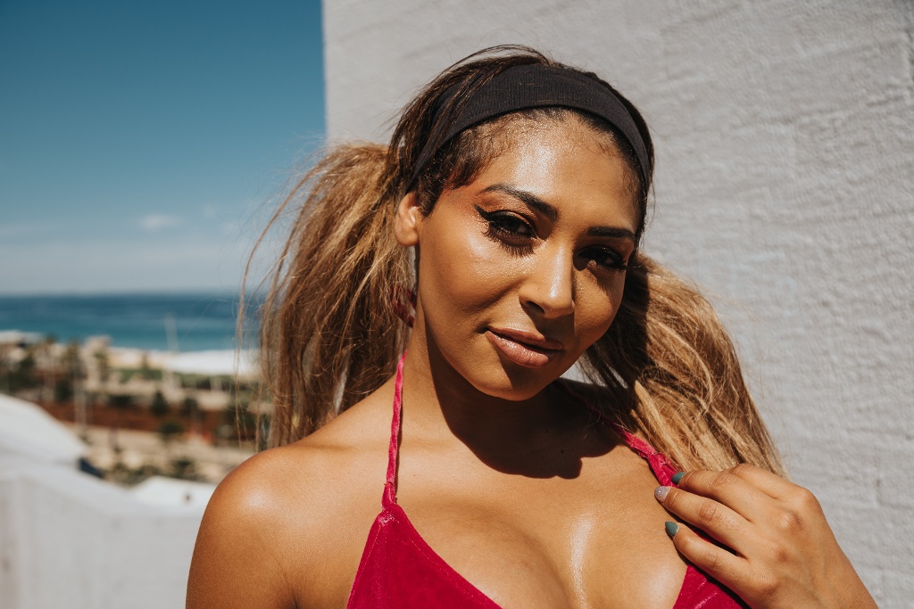 A person wearing a red top and black headband smiles while standing near the ocean.