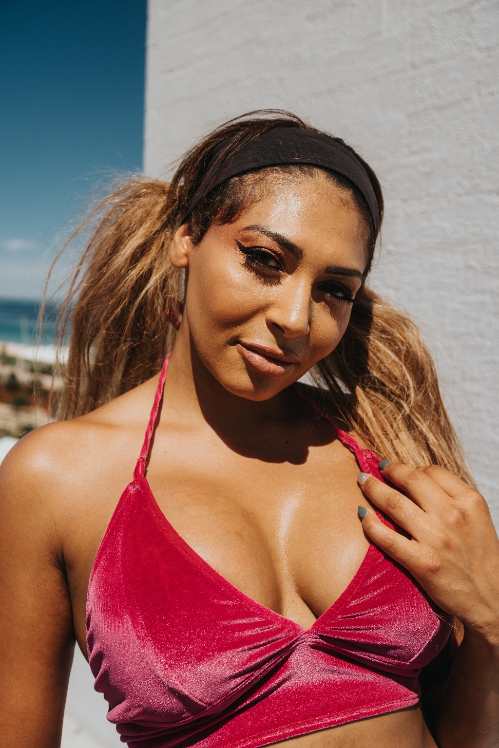 A person wearing a red velvet top and black headband poses outdoors against a bright background.